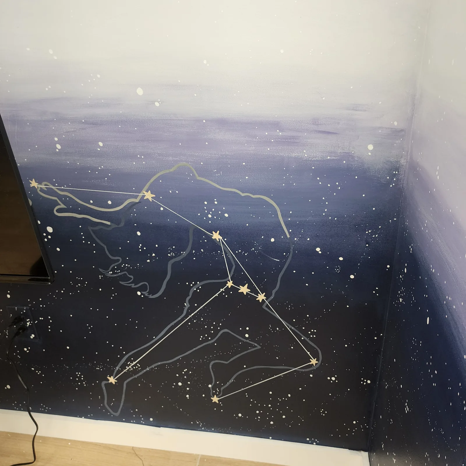 A leaping figure drawn as a constellation with gold stars on the dark blue mural in the corner of the room
