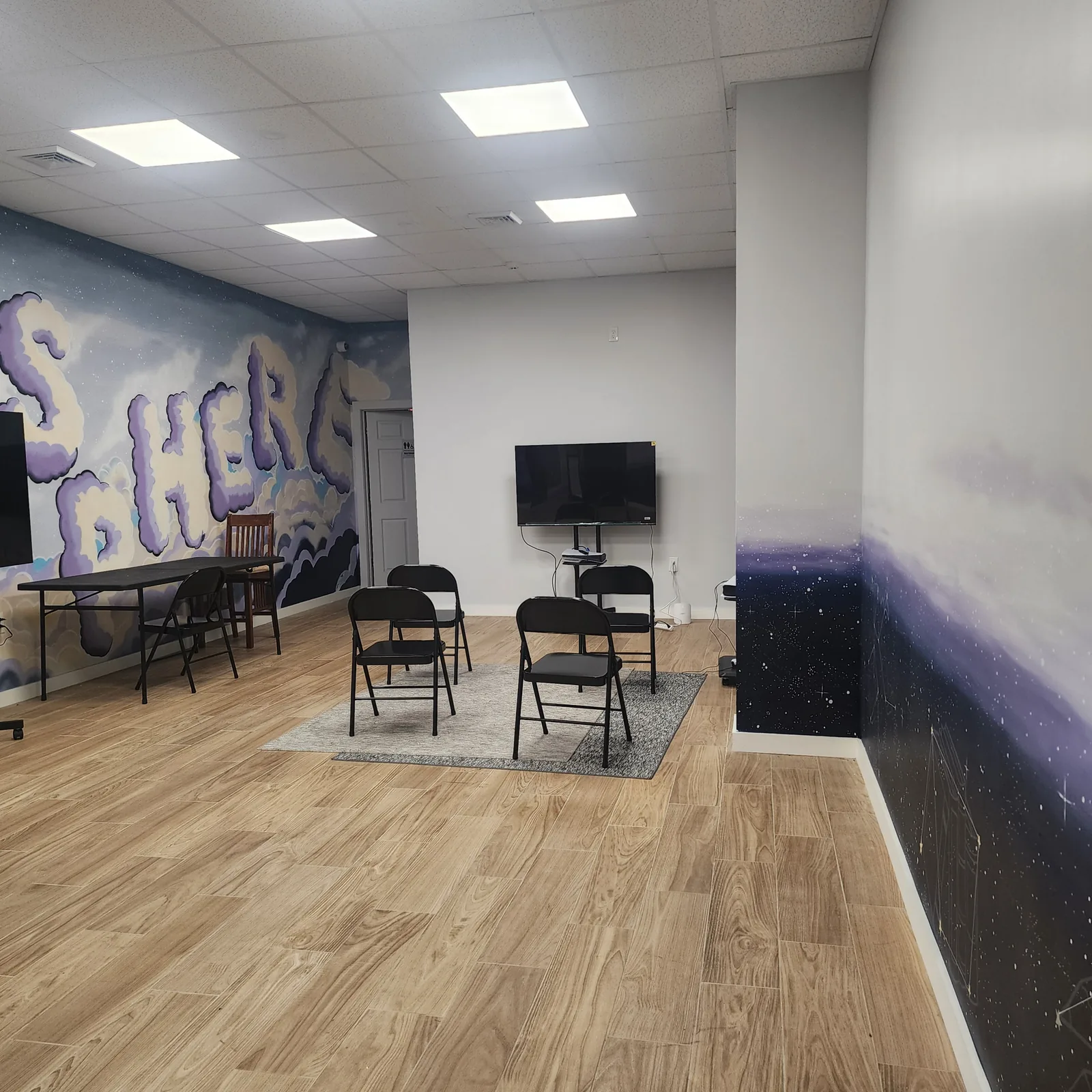 Folding chairs arranged on a rug facing a screen, beside the cloud mural and a folding table
